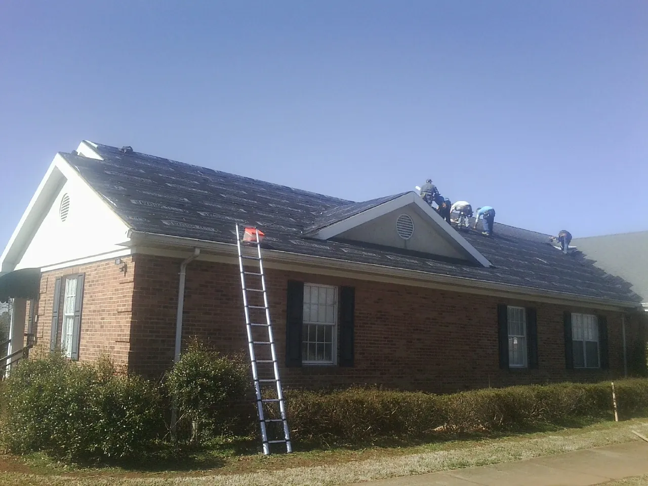Crew tearing shingles off a brick ranch roof with a ladder set — Emergency Roof Repair work by our crew in San Jose