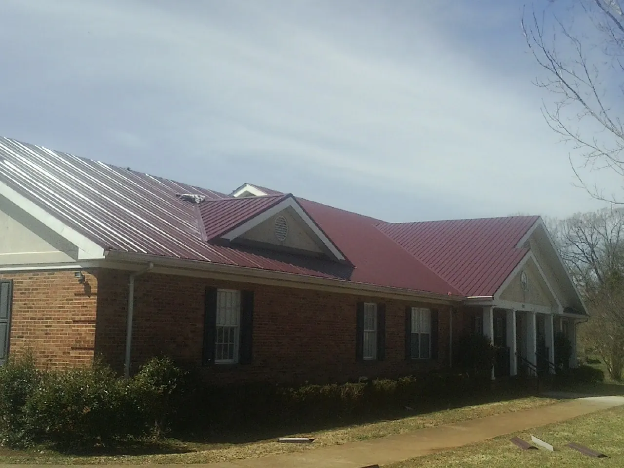 Red metal roof with gabled entries on a long brick building, from a Hail Damage Roof Repair job in San Jose